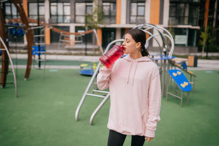 A young beautiful woman is drinking water on the playgroundの写真素材