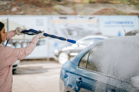 Brunette from a high-pressure hose applies a cleaner on the carの写真素材