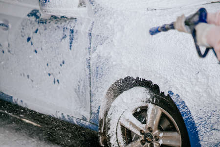 Brunette from a high-pressure hose applies a cleaner on the carの写真素材