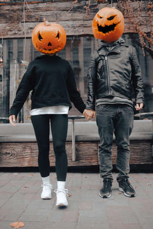 A guy and a girl with a pumpkin heads. Couple holding handsの写真素材