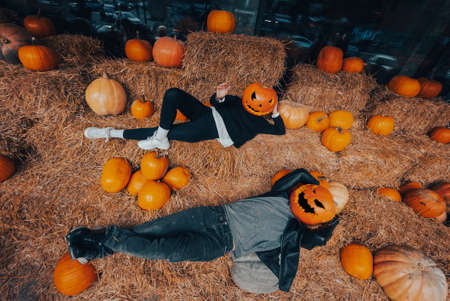 A guy and a girl with pumpkins on their heads are lying in the hayの写真素材