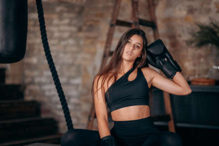 Beautiful young fitness girl posing at camera in black boxing gloveの写真素材