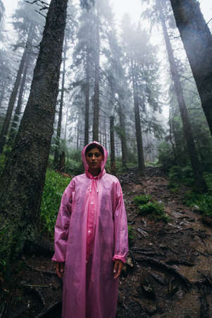 Young woman in a raincoat walks through the forest in the rainの写真素材