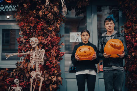 Couple holding pumpkin heads by the door on the streetの写真素材
