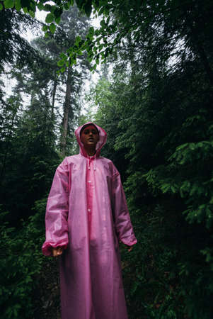 Young woman in a raincoat walks through the forest in the rainの写真素材