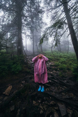 Young woman in a raincoat walks through the forest in the rainの写真素材