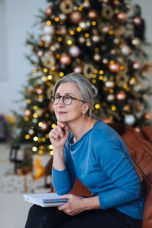 Happy senior woman in glasses thinking and writes in a diary homeの写真素材