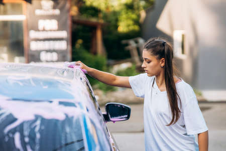 Brunette with two pigtails with a sponge washes the side of the carの写真素材