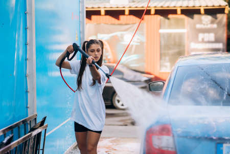 Brunette from a high-pressure hose washes the car at a car washの写真素材