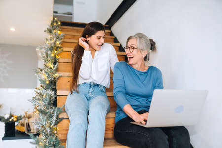 Mother and daughter sitting on the steps and watching something on laptop
