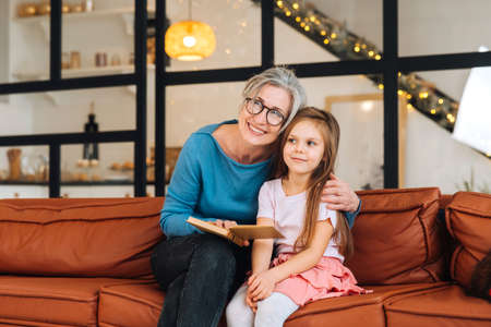Nice elderly woman grandmother reading story to granddaughter.の写真素材