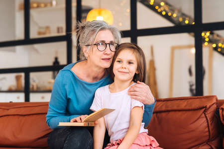 Nice elderly woman grandmother reading story to granddaughter.の写真素材