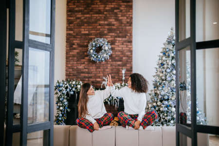 Two female student friends sitting on the couch at home. High fiveの写真素材