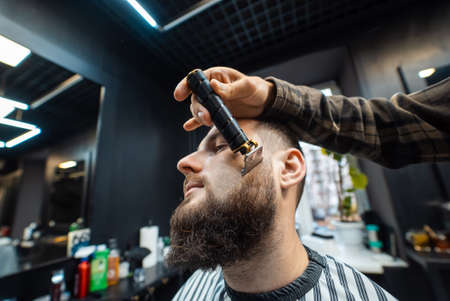 Barber works with a beard clipper. Hipster client getting haircut.の写真素材