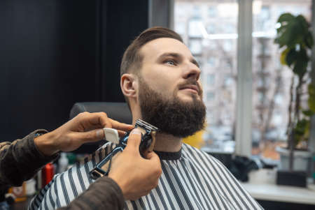 Barber works with a beard clipper. Hipster client getting haircut.の写真素材