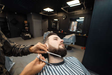 Hairdresser doing haircut of beard using comb and scissorsの写真素材