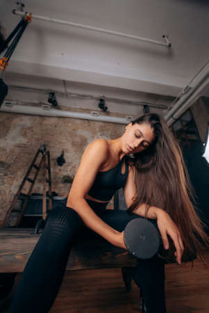 Young woman pumps up the muscles by one arm lifting dumbbell.の写真素材