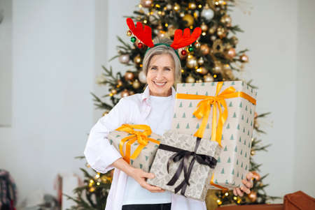 Grandma wearing deer christmas hat. Christmas presents in hands .の写真素材