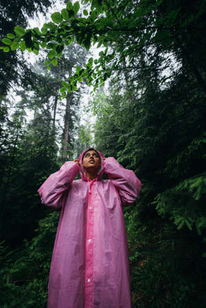 Young woman in a raincoat walks through the forest in the rainの写真素材