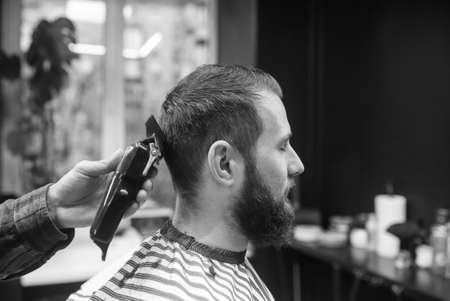 Master in barbershop makes mens haircutting with hair clipper
