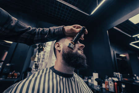 Barber works with a beard clipper. Hipster client getting haircut.の写真素材