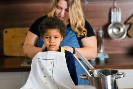 Mom ties an apron to her daughter in the kitchenの写真素材