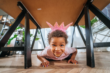 Little girl is playing under the table tongue in the cameraの写真素材