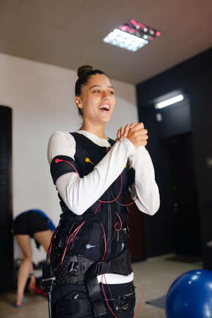 EMS training. Ecstatic girl performs exercises in a suit with cables.