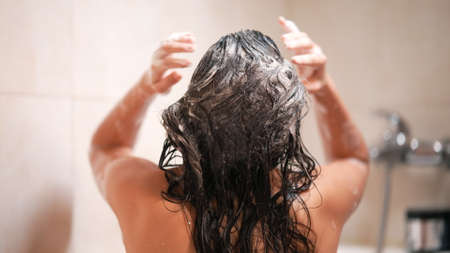 Woman takes a shower and shampoos her hair in the bathroomの写真素材
