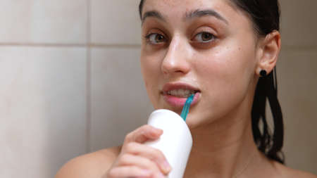 Smiling woman cleaning her teeth with oral irrigator.