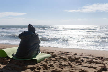 Pretty woman in warm clothes sitting on the cold autumn beach.の写真素材