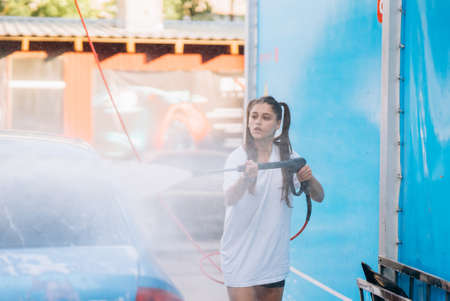 Brunette from a high-pressure hose washes the car at a car washの写真素材