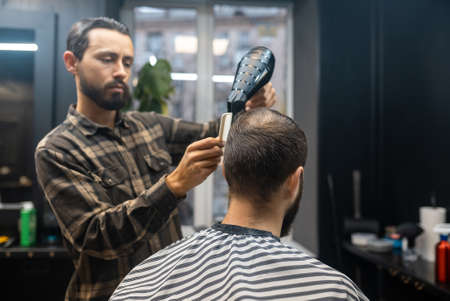 The master in the barbershop is styling the clients hairの写真素材