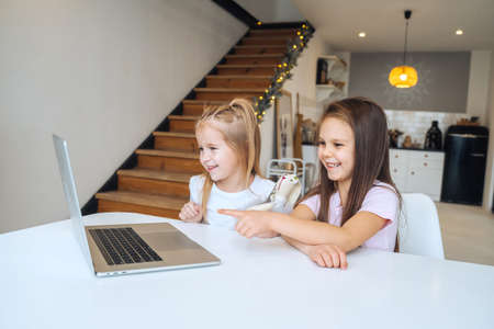 Two little girls playing together at the laptop while sitting at tableの写真素材