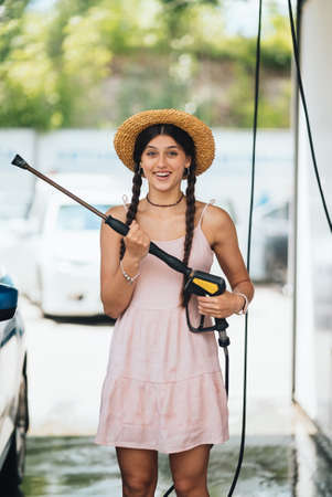 Woman with high pressure hose at car washの写真素材