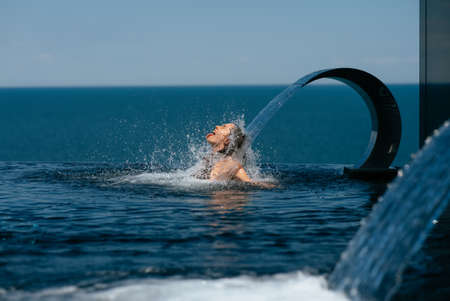 Young woman relaxing under swimming pool waterfall jetの写真素材