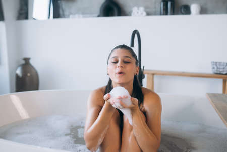 Young woman enjoys the foam while taking a bath