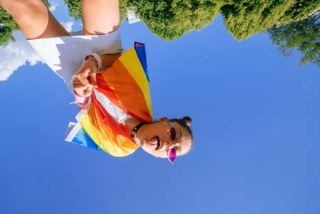 A young woman develops a rainbow flag against the sky