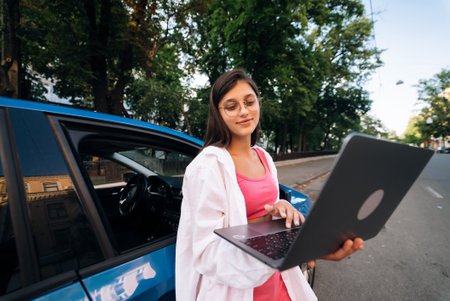 A young woman uses a laptop near a carの写真素材