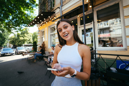 Smiling woman holding phone outdoors in cafe.の写真素材