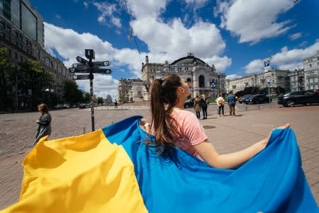 Young woman carries the flag of Ukraine fluttering behind herの写真素材