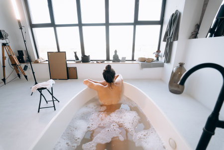 Relaxed lady taking bath, enjoying and relaxing while lying in bathtub, back viewの写真素材