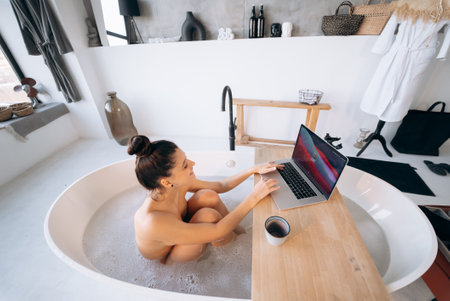 Young woman working on laptop while taking a bathtubの写真素材