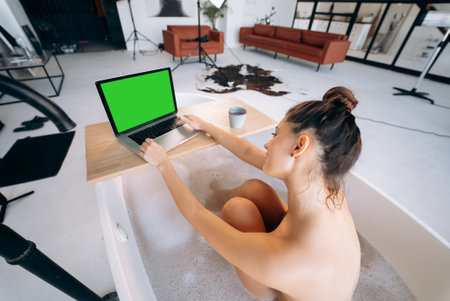 Young woman working on laptop while taking a bathtubの写真素材