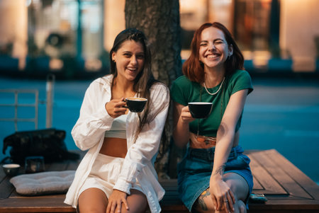 Best friends sitting on the park bench drinking coffee.の写真素材
