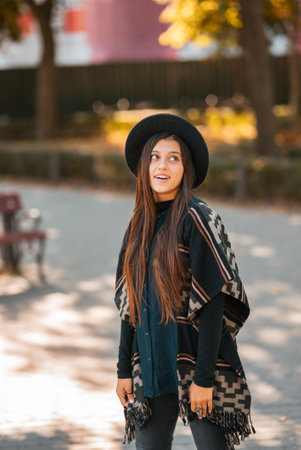 Stylish woman in poncho and hat enjoys autumns parkの写真素材