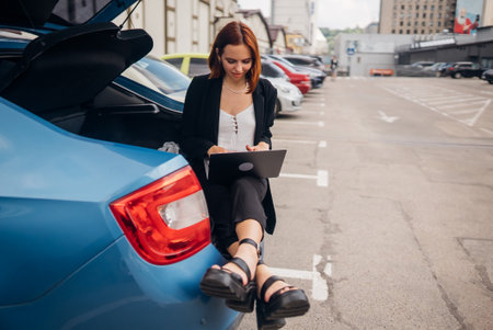 Woman working on laptop while sitting in trunk of carの写真素材