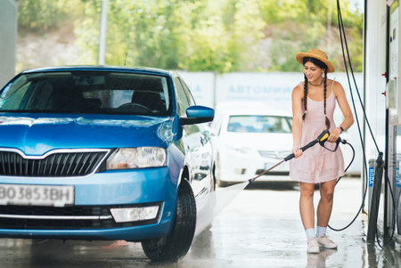 Brunette from a high-pressure hose washes the carの写真素材
