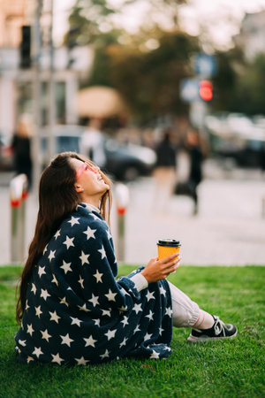 Young woman with a paper glass of coffee sitting on the grass
