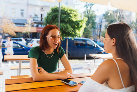 Two pretty girlfriends talking while sitting in a bar outdoorsの写真素材